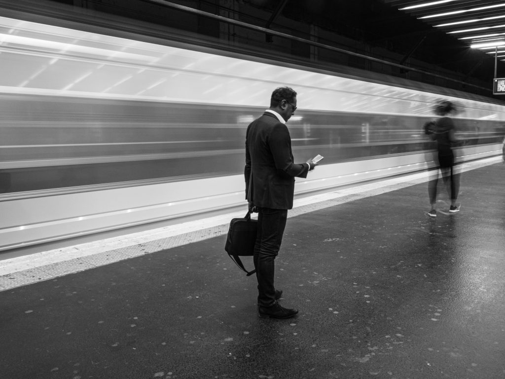 pexels-photo-32558696-32558696 Black and white photo of a businessman at a bustling Paris metro station, holding his phone.